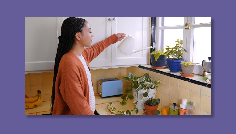 A pregnant woman waters plants in her kitchen.